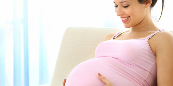 Pregnant woman sitting on couch holding stomach