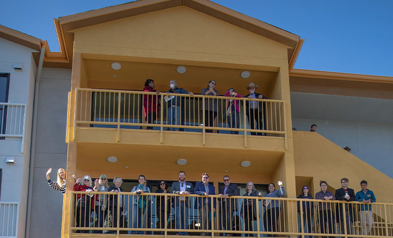 Numerous people waving from balconies of an apartment-style building.