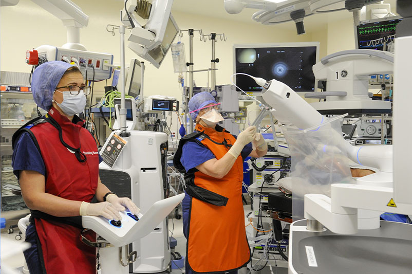 Two healthcare workers in scrubs assembling a robot in a hospital setting.